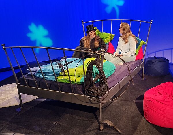 Moderatorin und eine Schornsteinfegerin, die zu Gast in der Sendung ist, sitzen auf einem Bett