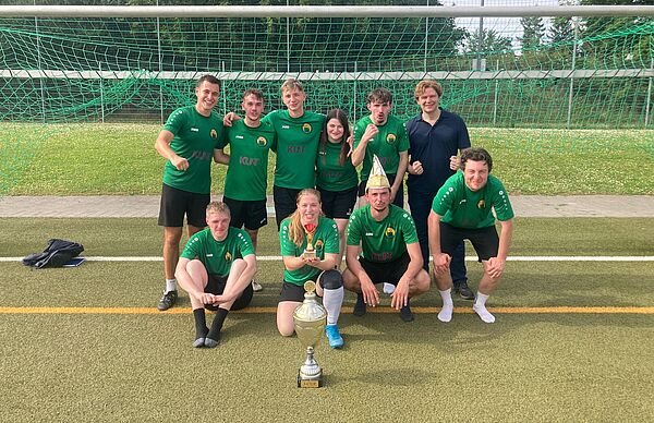 Die Mannschaft Hals und Steinbrecher posiert mit Michael Steinbrecher und Pokal vor dem Tor