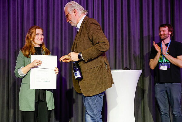 Herbert von Halem überreicht Eva-Maria Roese auf einer Bühne die Preisurkunde